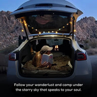 Tesla Model Y parked at a scenic campsite with camping gear and outdoor setup