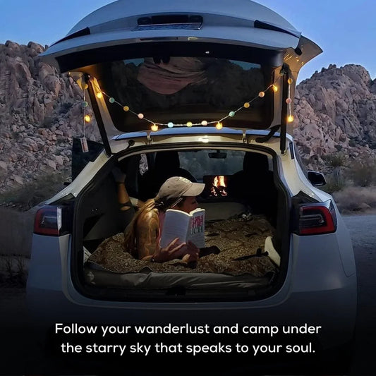 Tesla Model Y parked at a scenic campsite with camping gear and outdoor setup